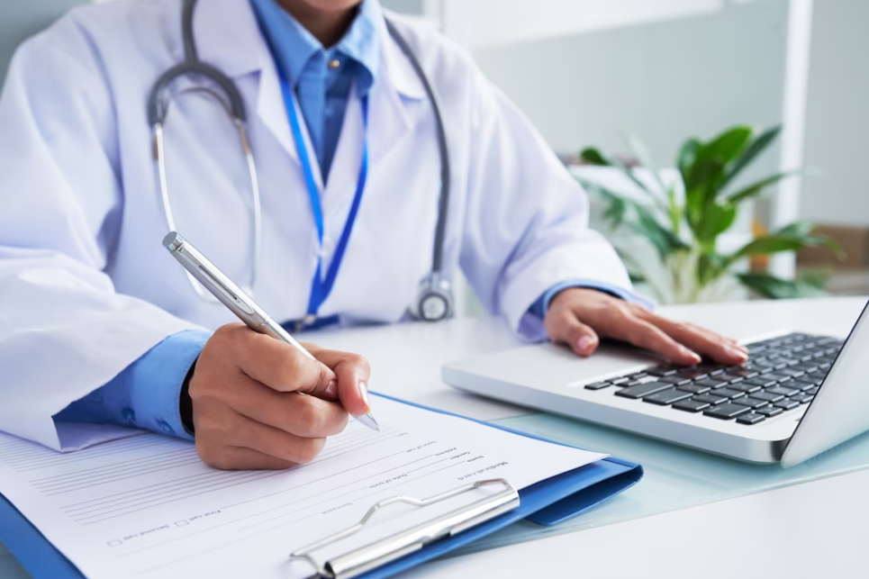 doctor writes on the sheet with a pen, and holds hand on the laptop keyboard